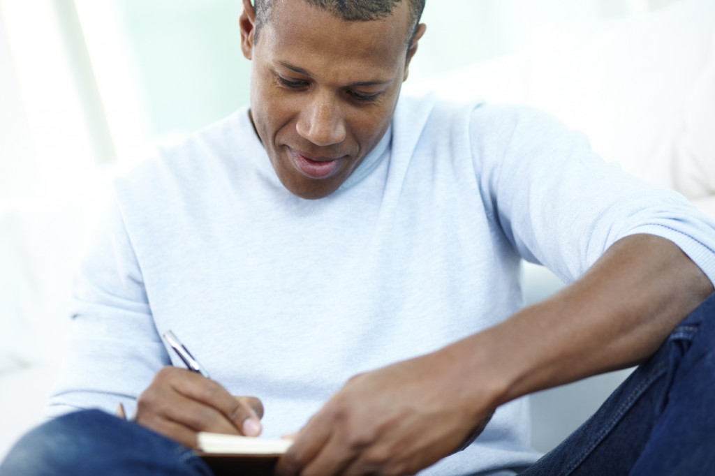 Image of young African man writing something in notepad