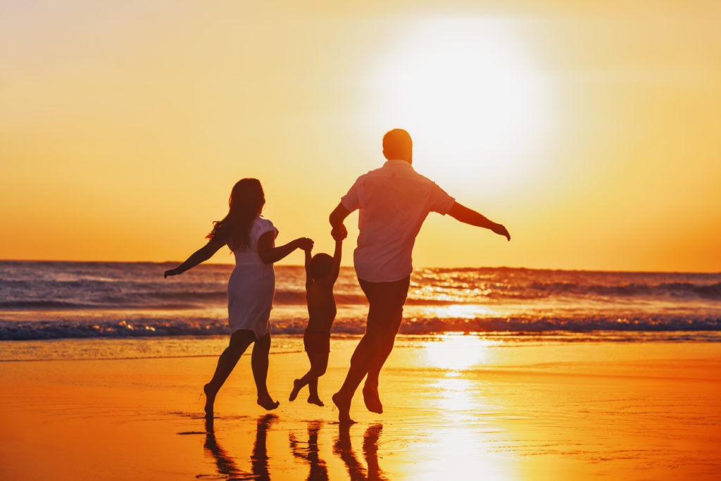 Happy family - father, mother, baby son hold hands and run with fun along edge of sunset sea on black sand beach. Active parents and people outdoor activity on tropical summer vacations with children.